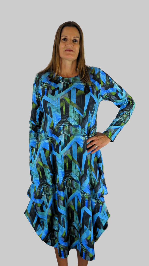 This hitch up dress is made from a soft feel jersey fabric, with an all over shades of blue print. The dress has a hitch up hem on both sides, which can be buttoned up or let down for a longer length. Perfect for any autumn / winter occasion from a wedding, mother of the bride, mother of the groom to a party or everyday wear. This dress will take you from day to night with effortless style and elegance. Available in Abstract Aqua, Fuchsia, Green & Fusion print and Aqua.